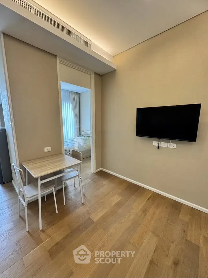 Modern apartment interior with wooden flooring, wall-mounted TV, and cozy dining area.