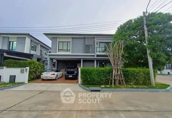 Modern two-story house with driveway and lush greenery in suburban neighborhood.