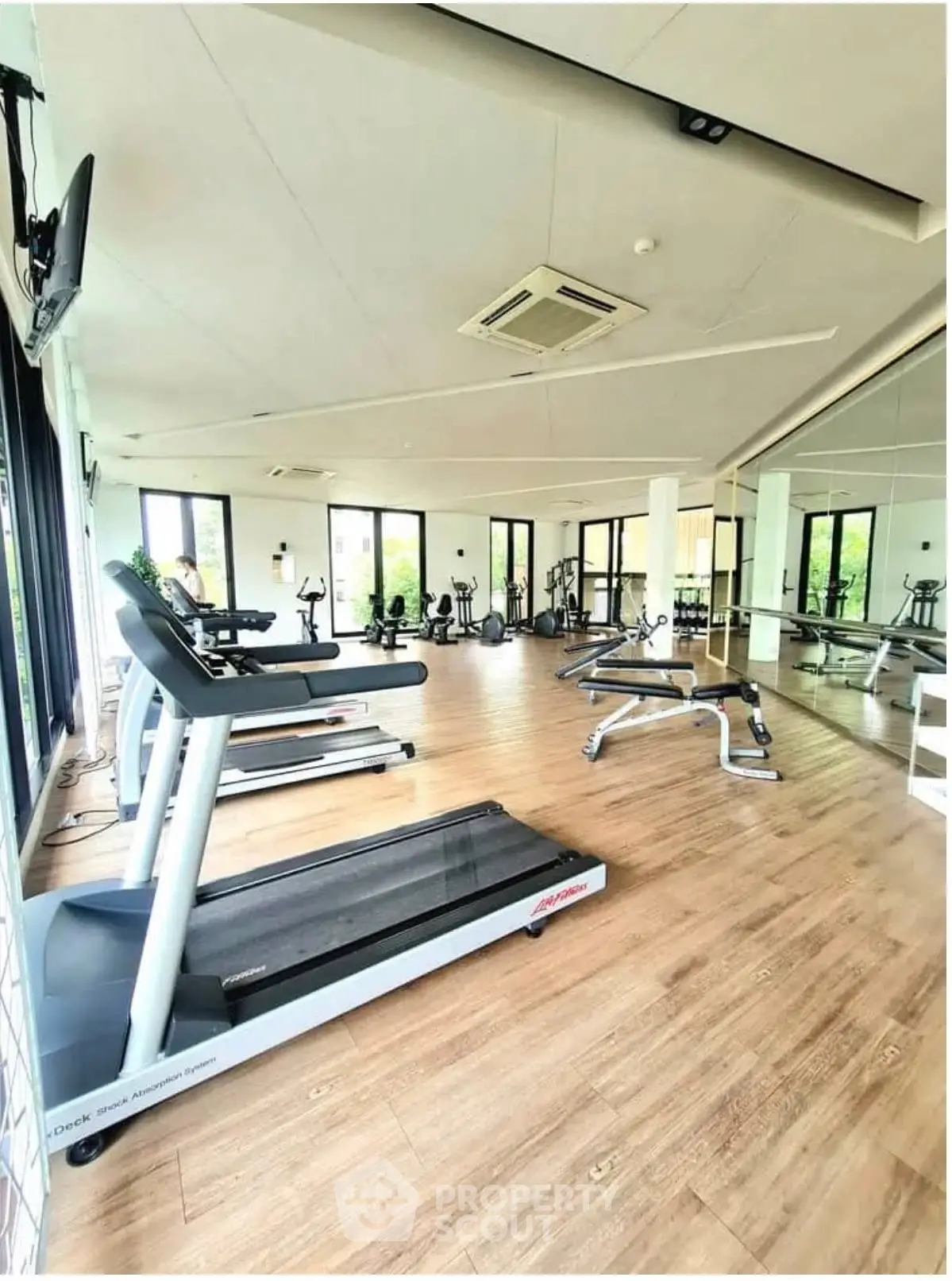 Spacious gym with modern equipment and large windows offering natural light.
