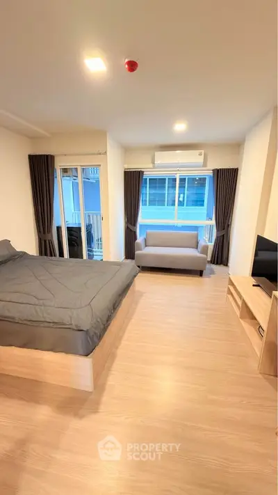 Modern studio apartment with cozy bed and stylish living area, featuring large windows and sleek wooden flooring.