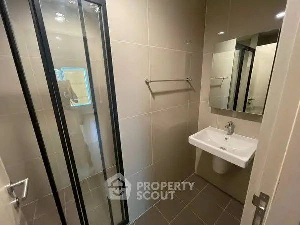 Modern bathroom with sleek shower and wall-mounted sink in a contemporary apartment.