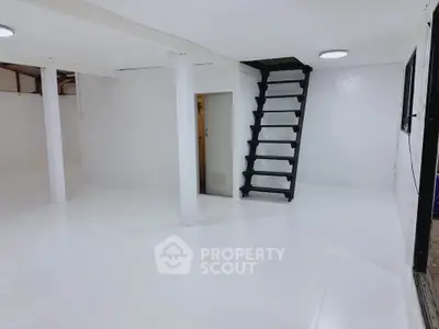 Spacious white basement with modern black staircase, ideal for storage or renovation.