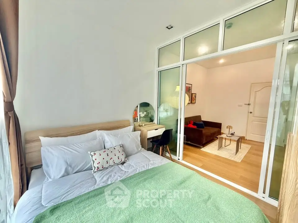 Modern bedroom with glass partition to cozy living room, featuring stylish decor and natural light.