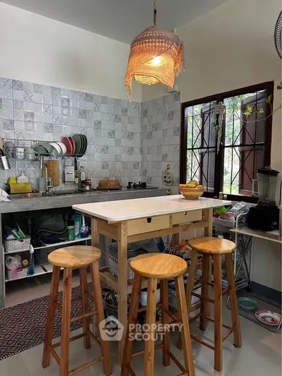 Charming kitchen with open layout and rustic wooden stools, featuring a cozy pendant light and tiled backsplash.