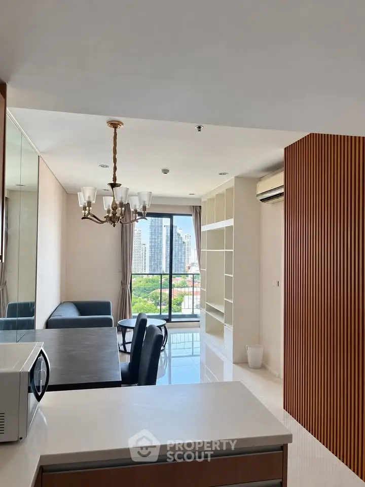 Modern living room with city view, elegant chandelier, and open layout in high-rise apartment.