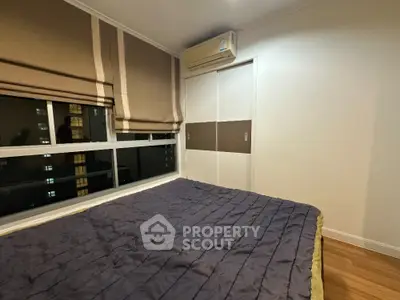 Cozy bedroom with large windows offering a city view, modern air conditioning unit, and elegant wooden flooring, perfect for urban living.