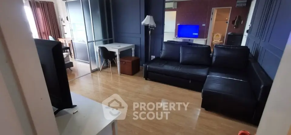 Spacious living room with modern black leather sofa and wooden flooring