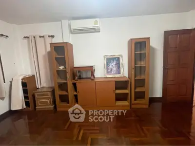 Spacious living room with wooden flooring and built-in cabinets, featuring air conditioning and elegant decor.