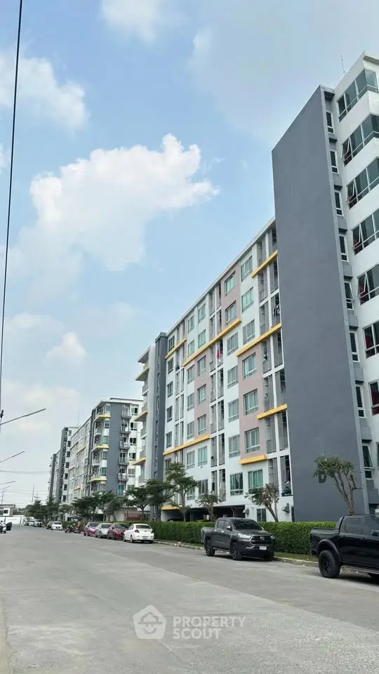 Modern apartment buildings with street view and parked cars under a clear blue sky.