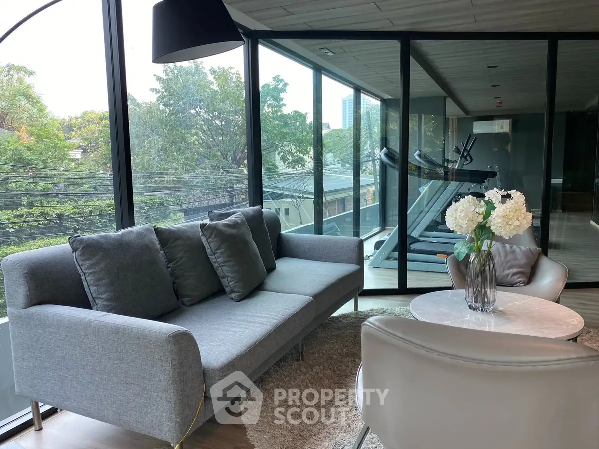 Modern living room with large windows and gym view, featuring stylish sofa and elegant decor.