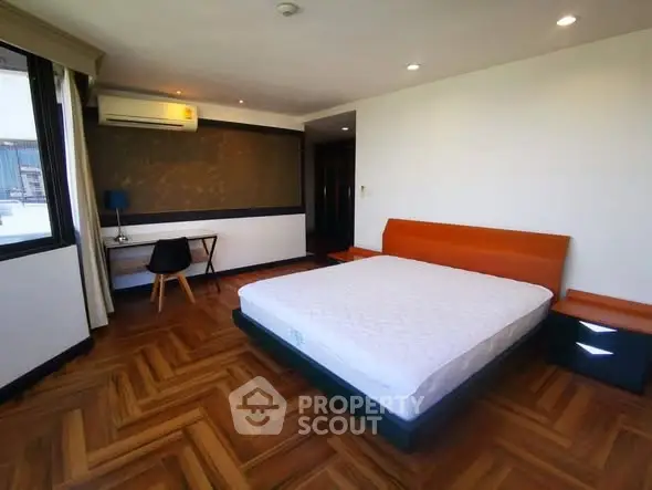 Spacious bedroom with modern design and wooden flooring, featuring a cozy bed and study area.