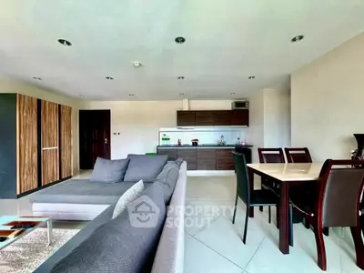 Spacious open-plan living room with modern kitchen and dining area, featuring sleek furniture and ample natural light.