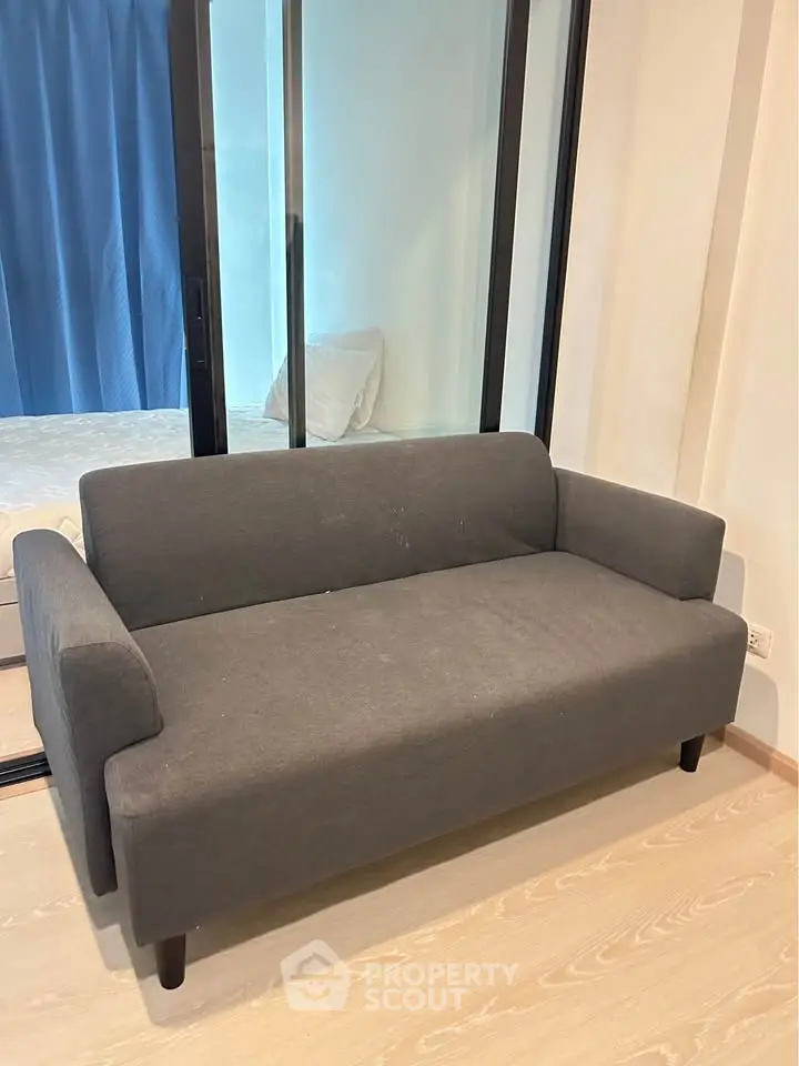 Modern living room with sleek gray sofa and glass partition, showcasing minimalist design and cozy ambiance.
