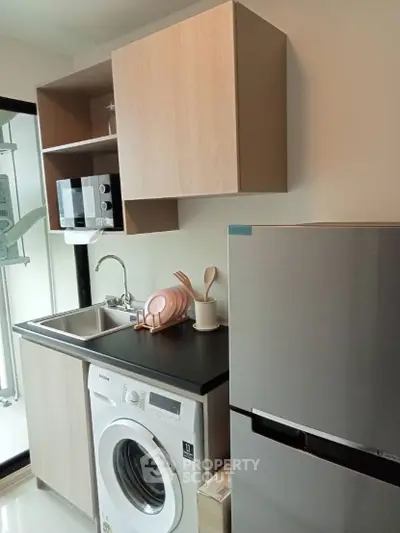 Modern kitchen with washing machine, microwave, and sleek cabinetry in compact layout.