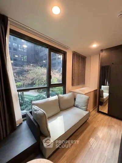 Cozy living room with large window overlooking garden, featuring a comfortable sofa and wooden flooring.