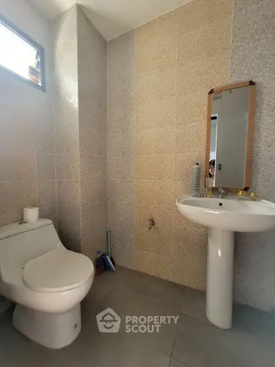Modern bathroom with pedestal sink and tiled walls, featuring a sleek toilet and small window.