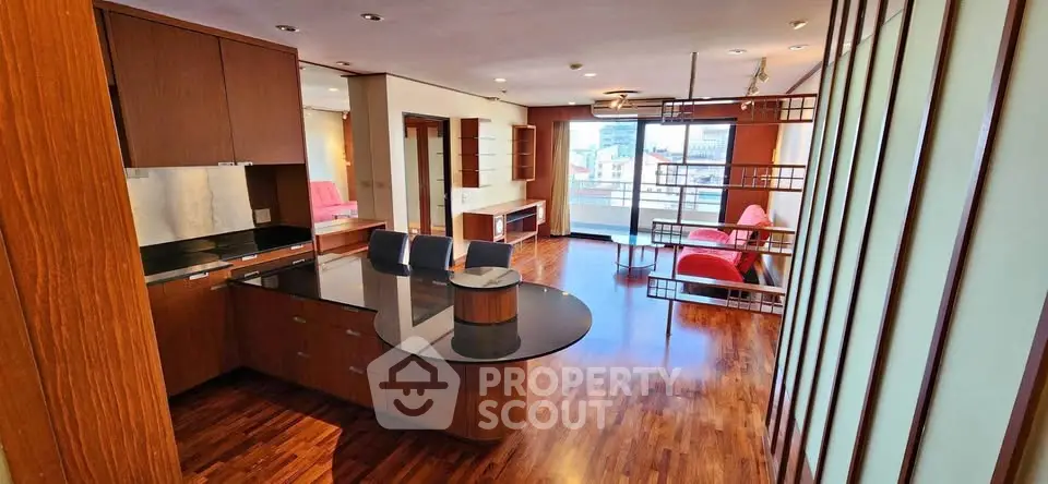 Spacious modern living room with open kitchen and balcony view, featuring sleek wooden flooring and stylish furniture.