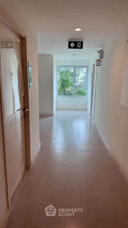 Bright corridor with emergency exit sign and window view in modern building.