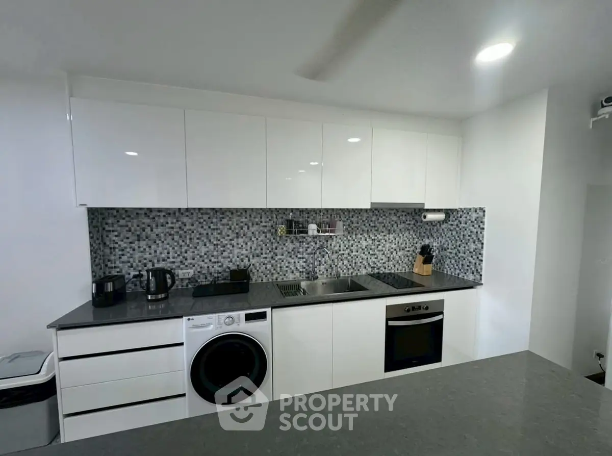 Modern kitchen with sleek white cabinets, mosaic backsplash, and integrated appliances.