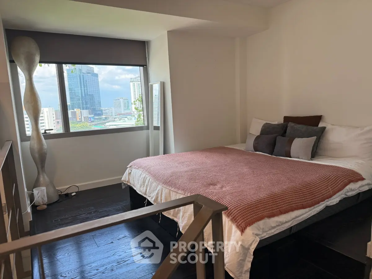 Modern bedroom with city view, featuring stylish decor and large window for natural light.