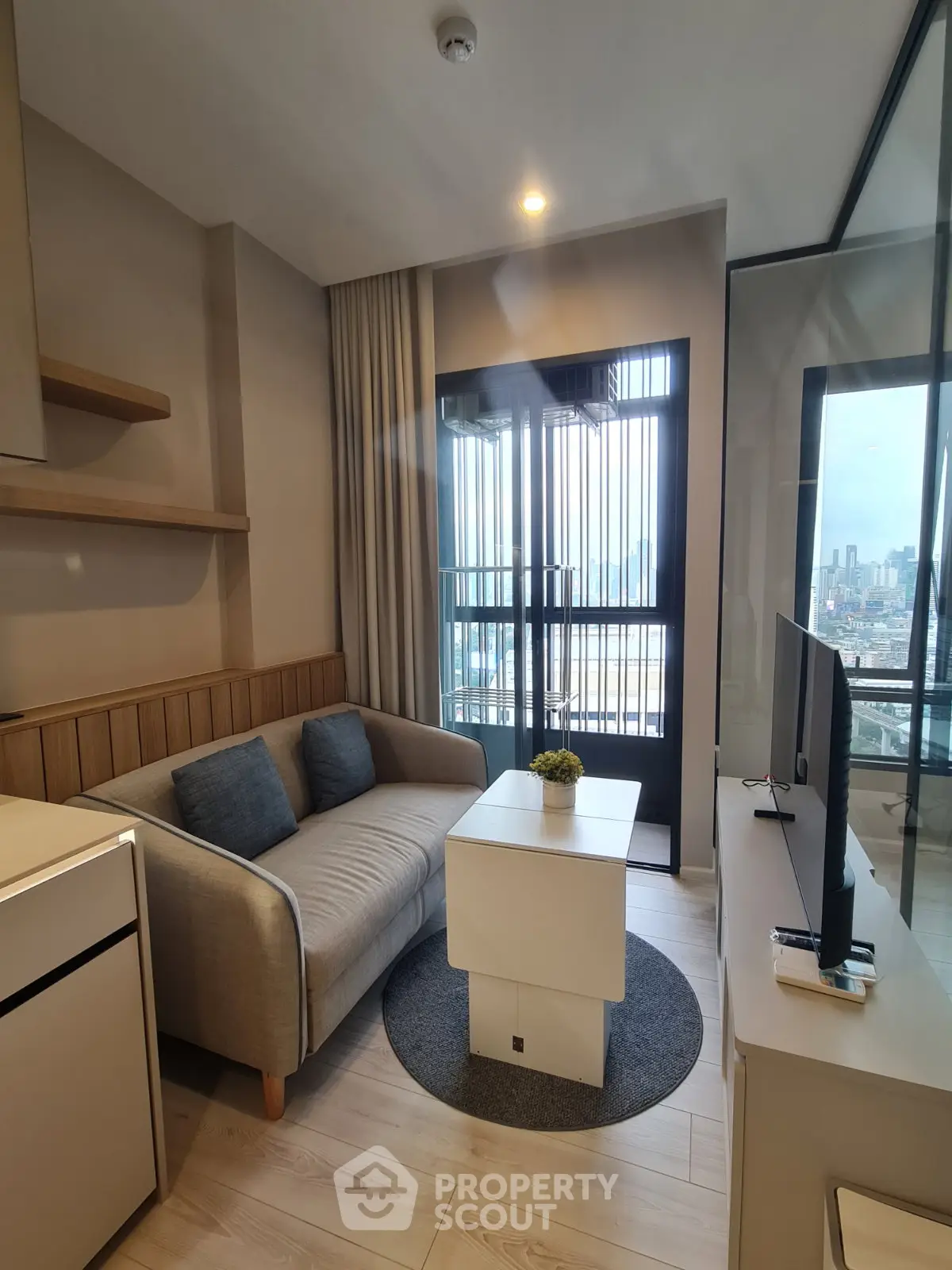 Modern living room with city view, cozy sofa, and sleek TV setup in a stylish apartment.
