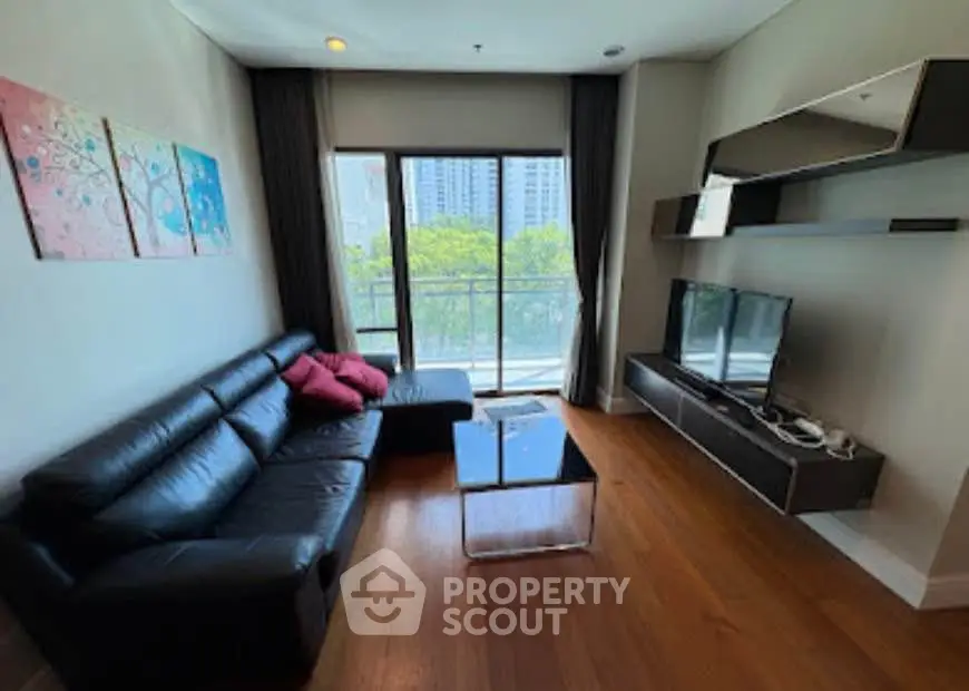 Modern living room with sleek black sofa, wall-mounted TV, and balcony view in urban apartment.