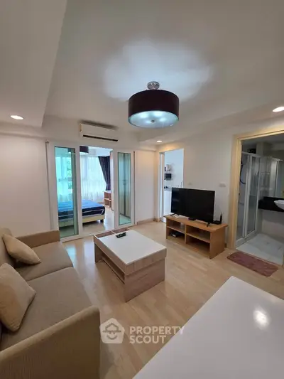 Modern living room with cozy sofa, TV, and access to bedroom, showcasing open layout and stylish lighting.