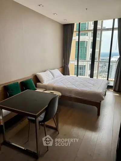 Modern bedroom with large windows and city view, featuring a cozy bed and stylish furniture.