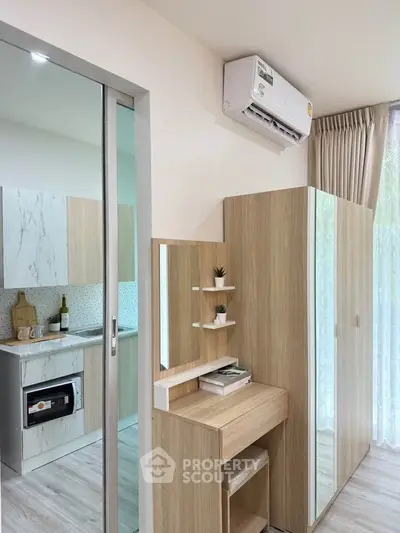 Modern apartment interior with sleek kitchen and stylish wooden furniture, featuring a compact workspace and air conditioning.