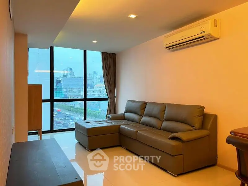 Modern living room with large window and city view, featuring a comfortable sofa and air conditioning.