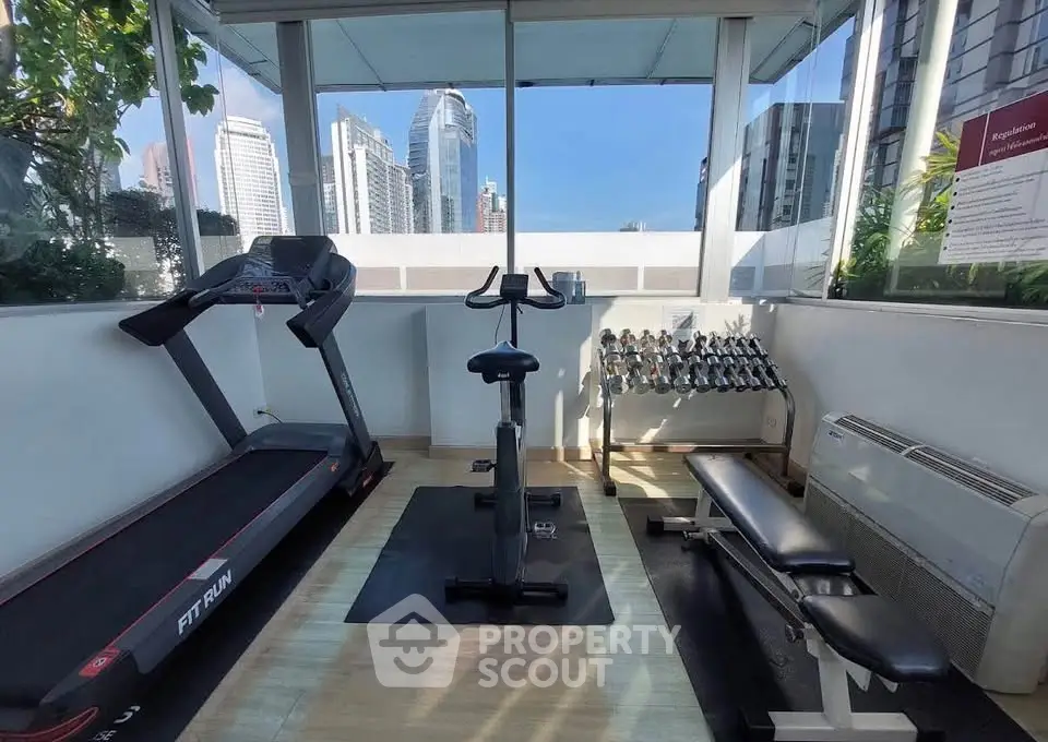 Modern gym with city view featuring treadmill, exercise bike, and weights