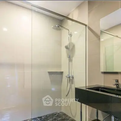 Modern bathroom with glass shower and sleek black sink in contemporary design.
