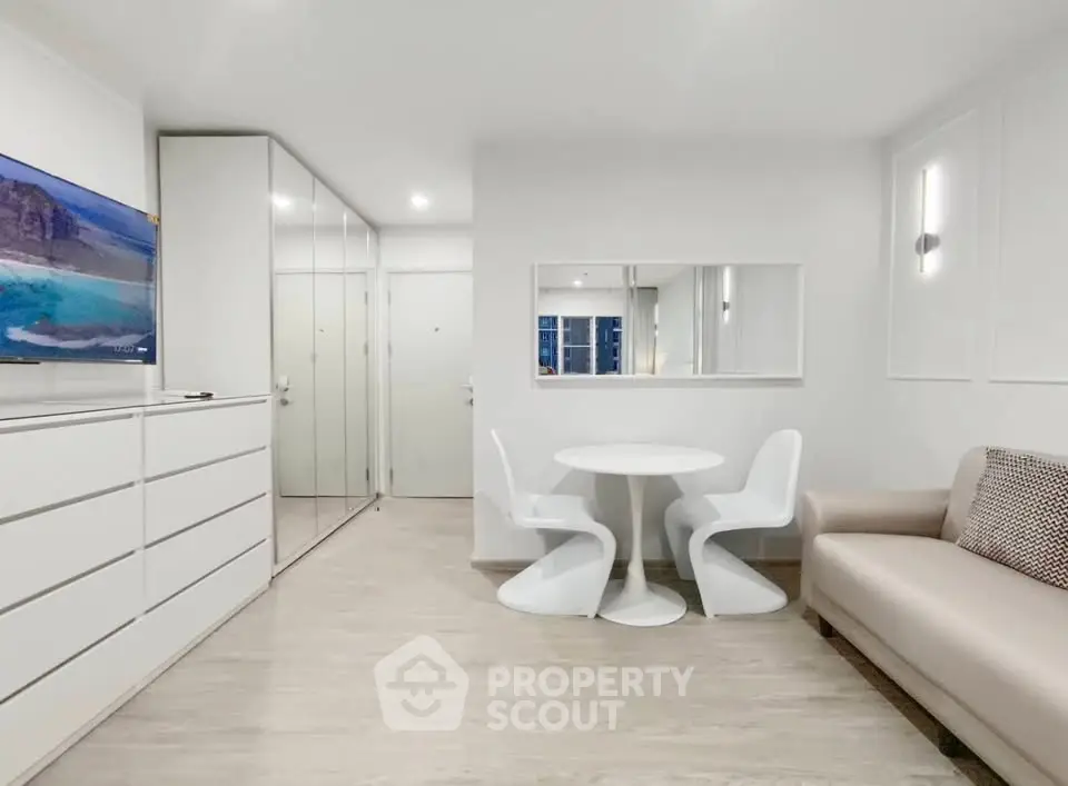 Modern minimalist living room with sleek white furniture and mirrored closet doors.