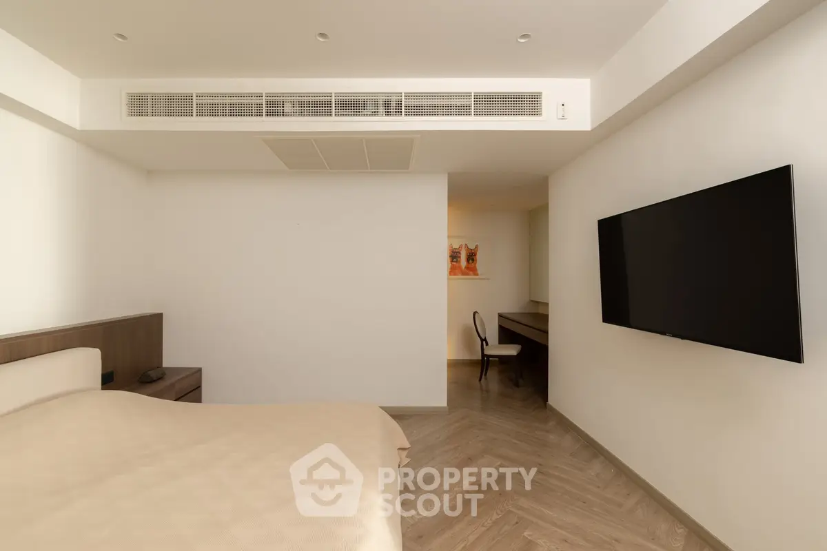 Modern bedroom with sleek design, featuring a wall-mounted TV and stylish wooden flooring.