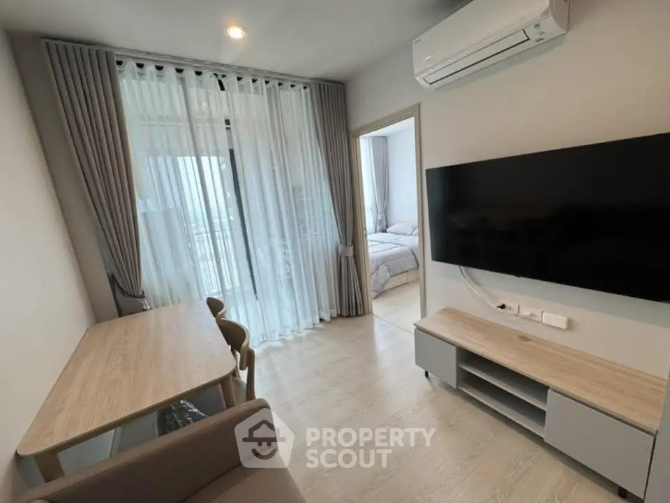 Modern living room with sleek furniture and large TV, featuring a view into a cozy bedroom.