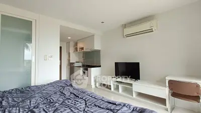 Modern studio apartment with sleek design, featuring a cozy bed, TV, and compact kitchen area.