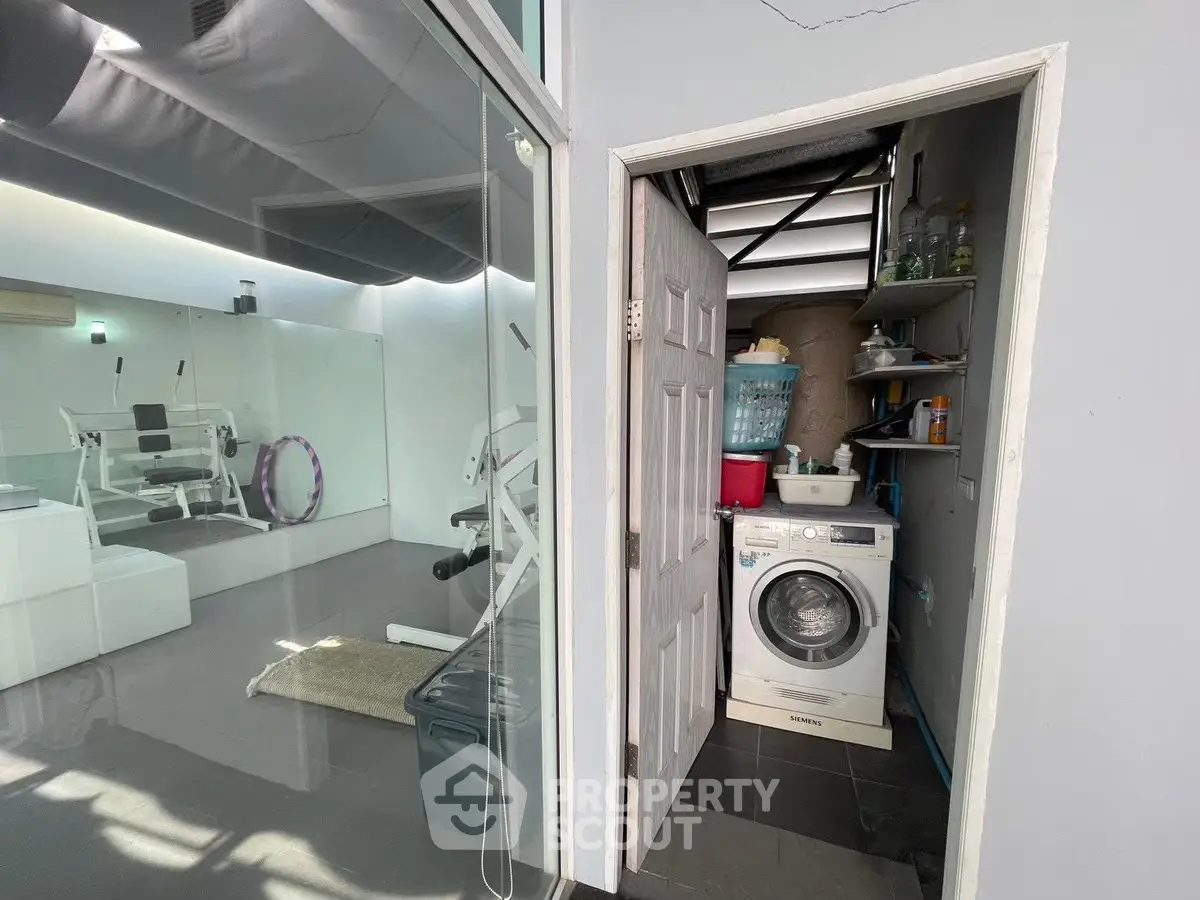 Modern gym with adjacent laundry area featuring washing machine and storage shelves.