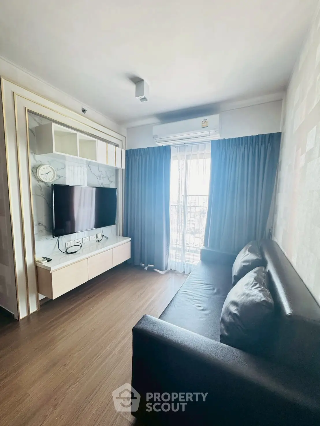Modern living room with sleek sofa and wall-mounted TV, featuring large window with curtains.
