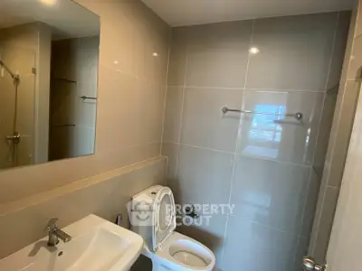 Modern bathroom with sleek fixtures and neutral tiles, featuring a toilet, sink, and mirror.