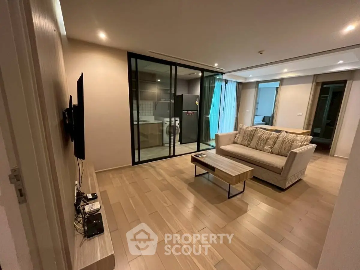 Modern living room with open layout and sleek kitchen view, featuring stylish furniture and wooden flooring.