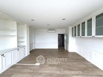 Spacious empty living room with wooden flooring and built-in cabinets.