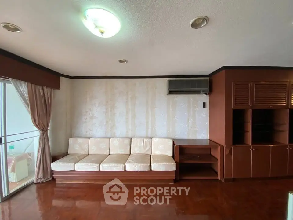 Spacious living room with elegant wooden flooring and built-in storage, featuring a cozy sofa and balcony access.