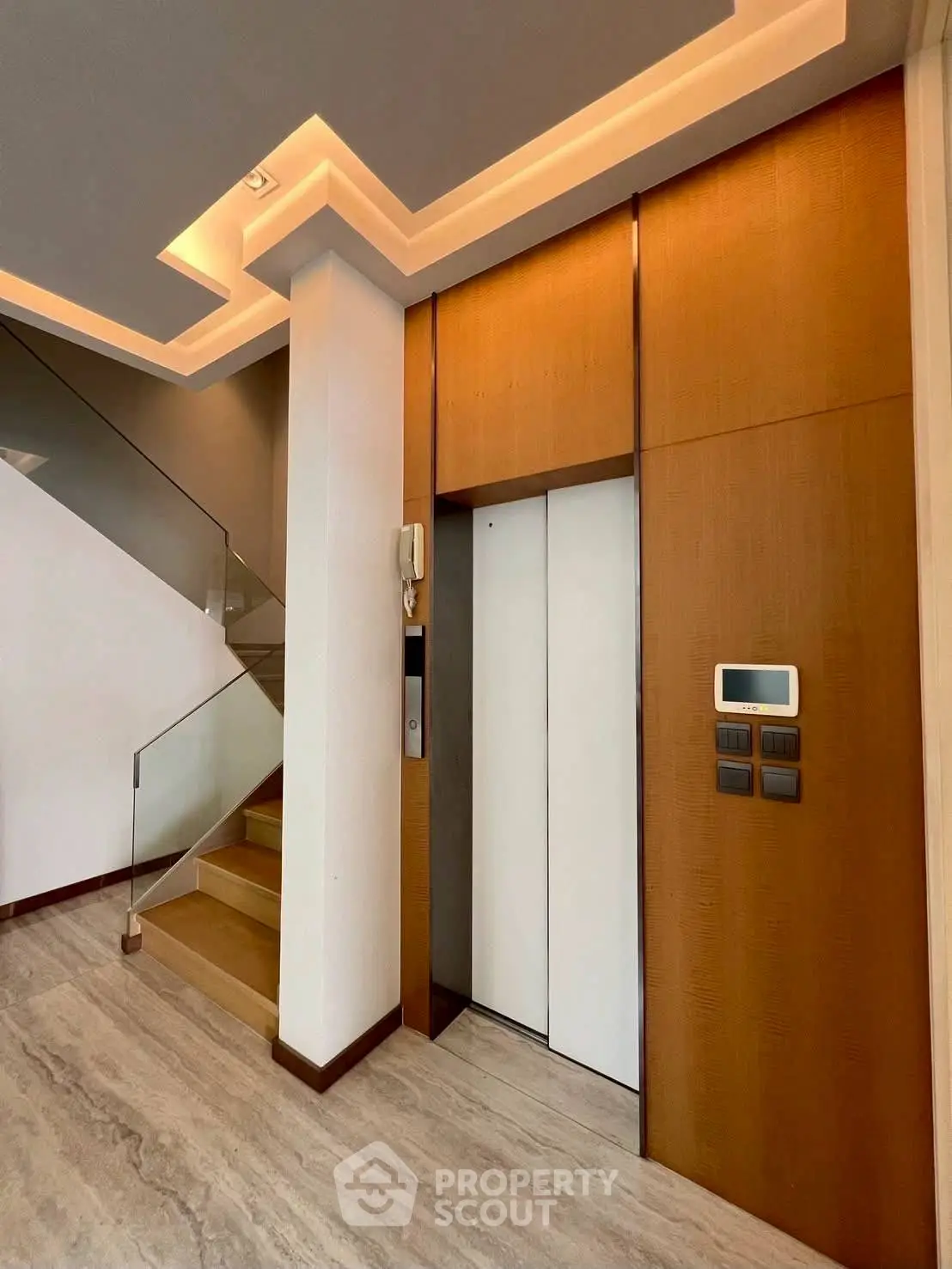Modern elevator entrance with sleek wooden paneling and stylish staircase in luxury building.