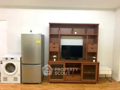 Modern living room with wooden entertainment center, fridge, and washing machine on hardwood floor.