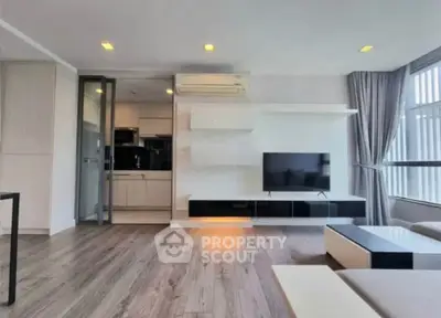 Modern living room with sleek design and open kitchen layout, featuring large windows and stylish furniture.