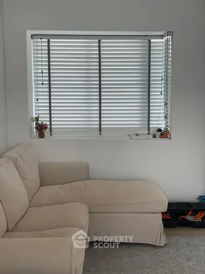 Cozy living room with beige sofa and window blinds, perfect for relaxation.