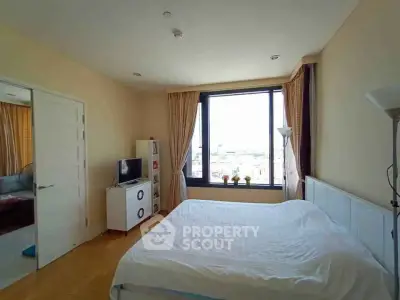 Spacious bedroom with large window offering city views, modern decor, and cozy ambiance.