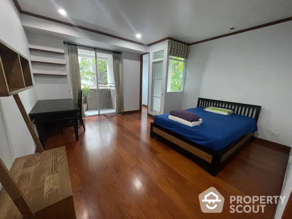 Spacious bedroom with wooden flooring and balcony access in modern apartment.