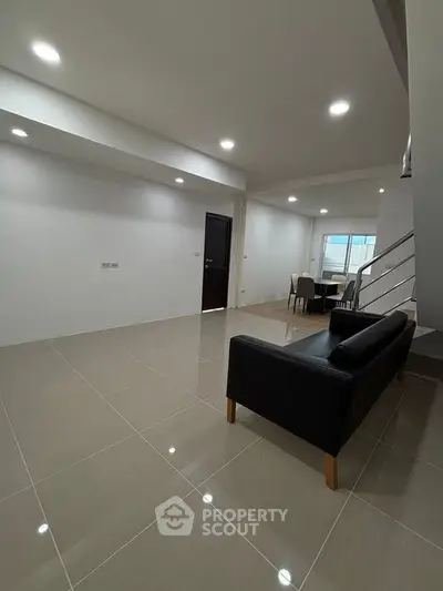 Spacious modern living room with sleek black sofa and dining area, perfect for contemporary living.