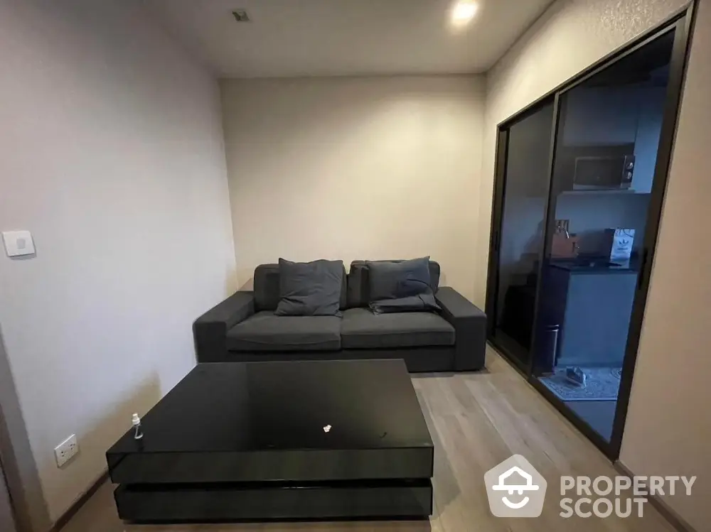 Cozy living room with modern sofa and glass coffee table, adjacent to a compact kitchen area.